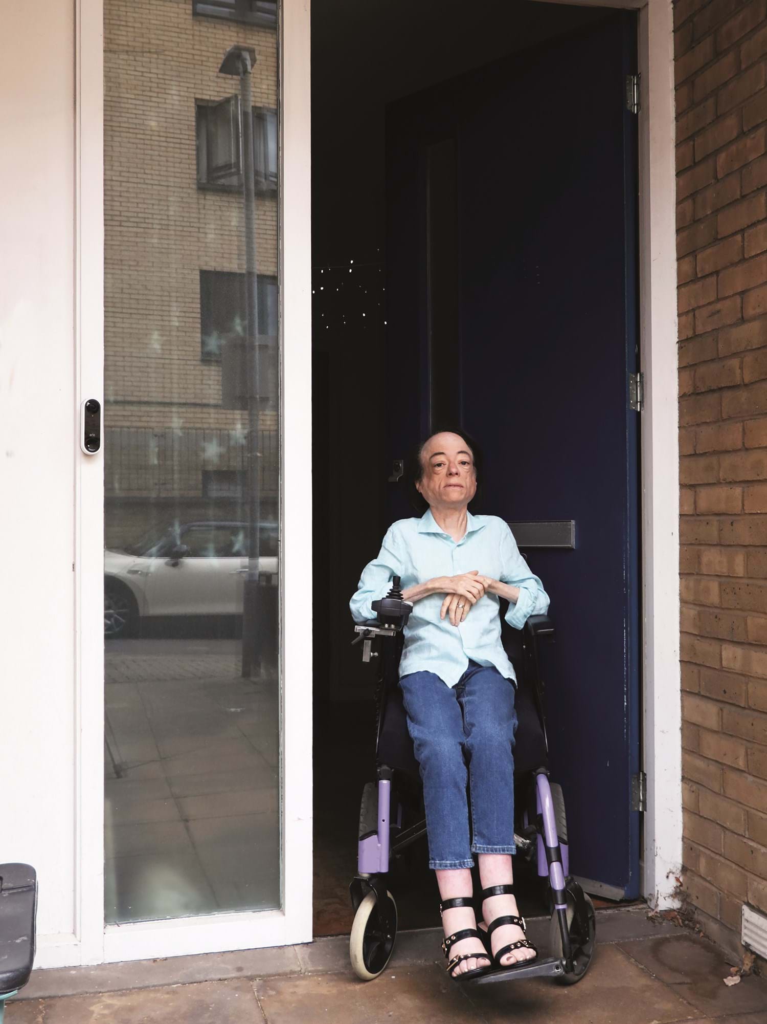 Photo of a person in a blue shirt and jeans, in a wheelchair outside their porch door
