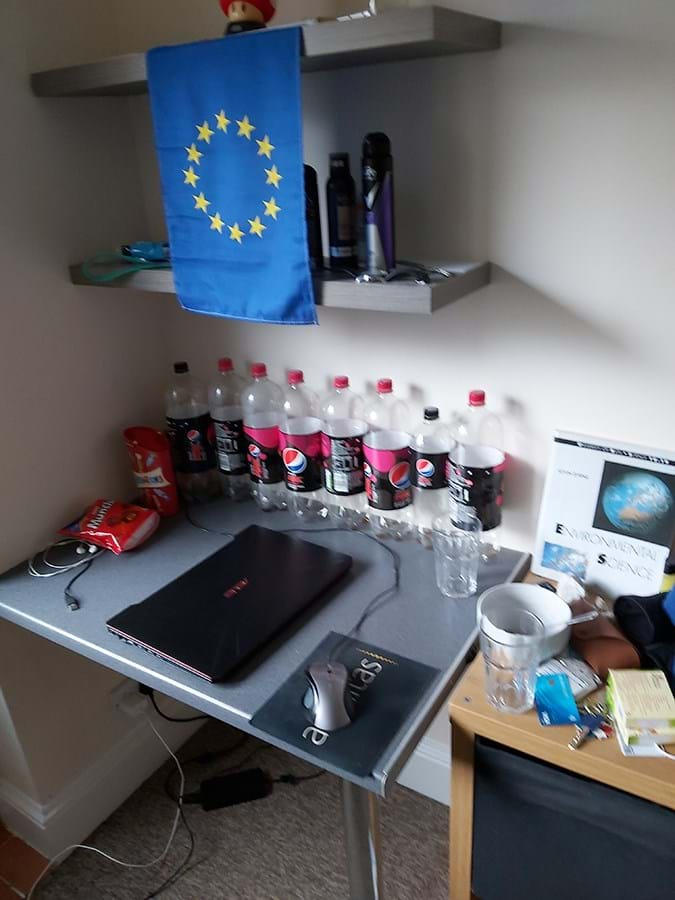 Empty soft drink bottles lined up on a desk next to a closed laptop