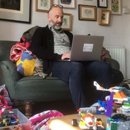 Two children playing with toys on the floor while an adult uses a laptop on the sofa