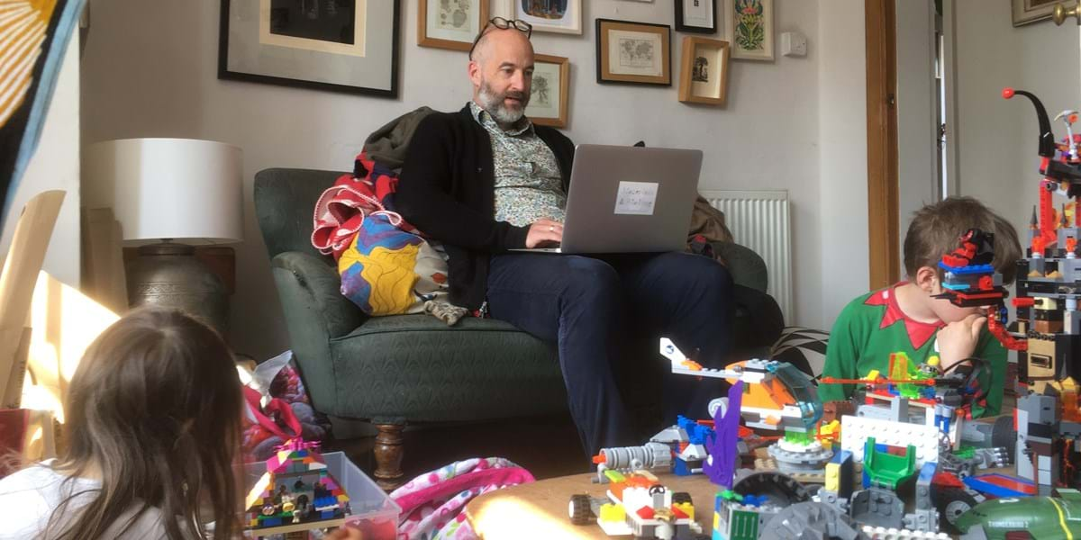 Two children playing with toys on the floor while an adult uses a laptop on the sofa