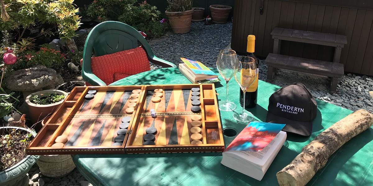 A garden table set with a game of backgammon, a book and a bottle of wine
