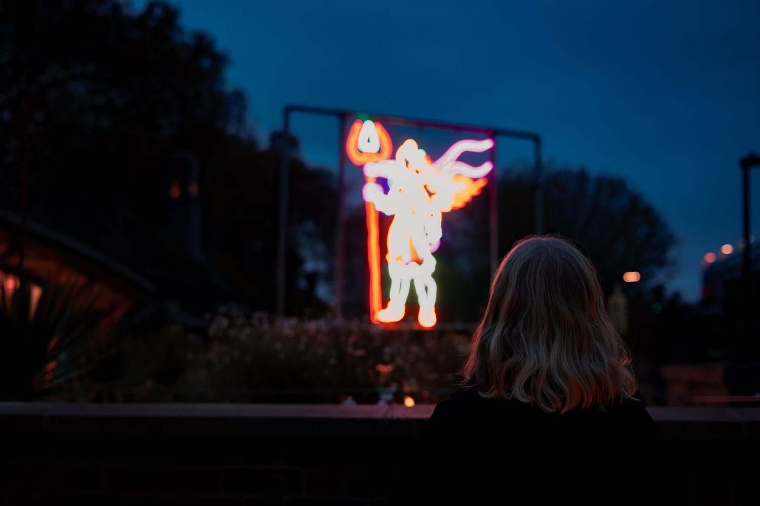 The back of a person as they observe a large multicoloured neon light structure before them