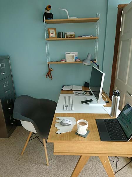 Home office with an open laptop, extra screen and shelves behind