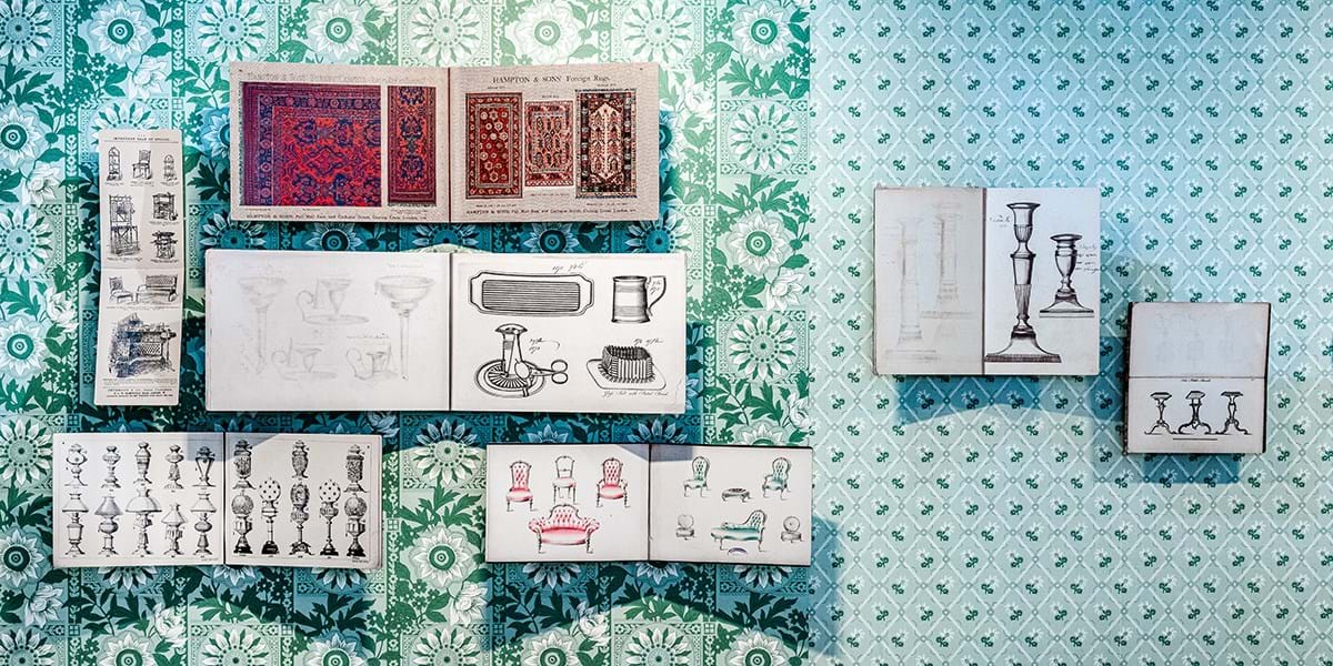 Images from a furniture catalogue hung on a wall covered with pale blue, patterned wallpaper