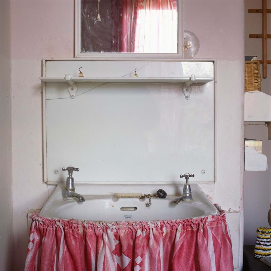 A mirror over a sink with a pink curtain