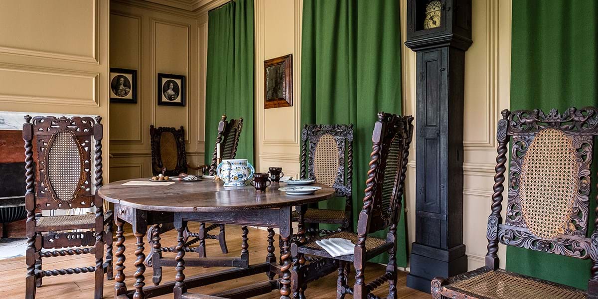 Room setting with wooden table and chairs, floor-standing clock and green curtains
