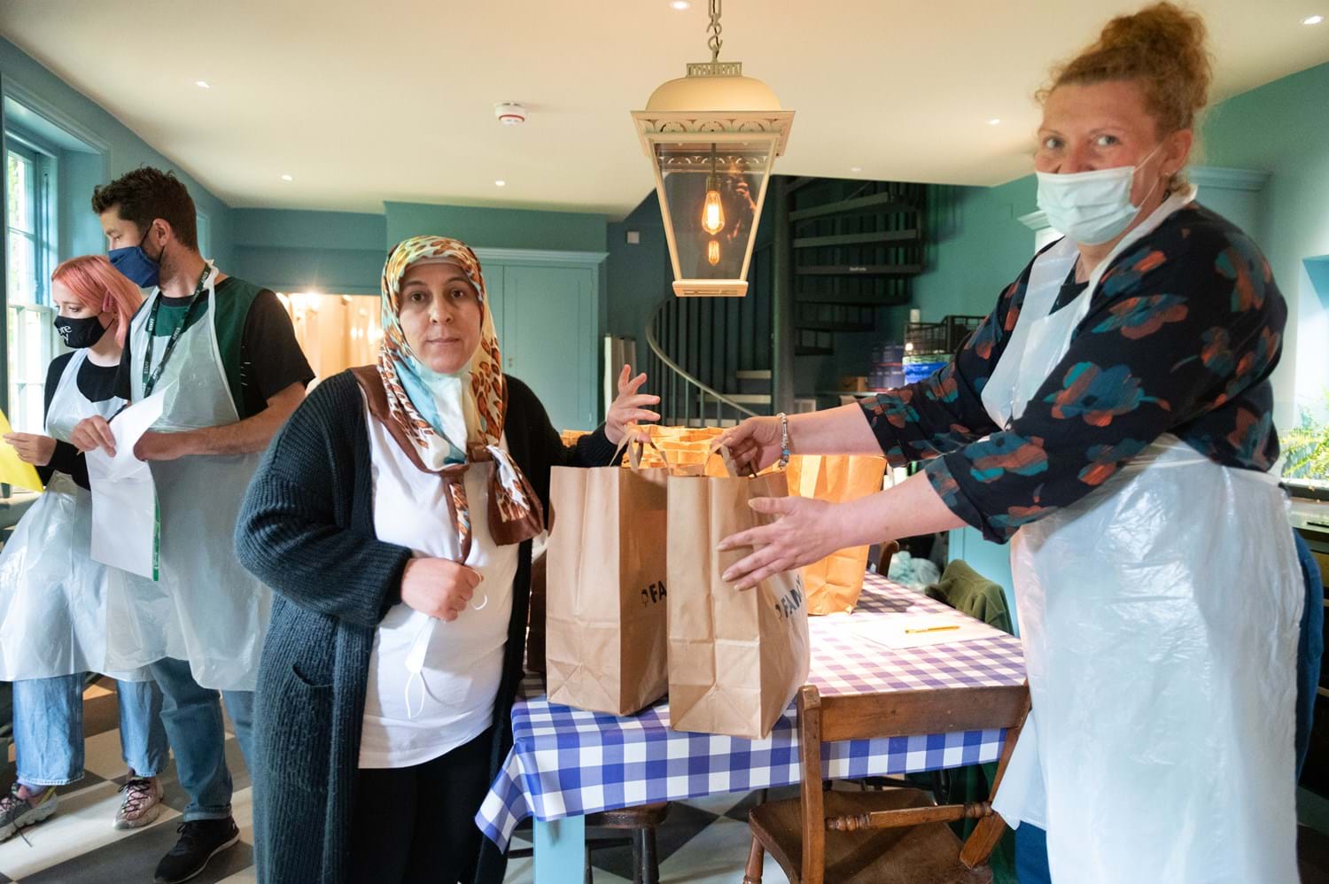 A person passing full paper bags to another person inside a kitchen