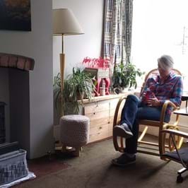 person sat in chair in living room with fireplace and plants