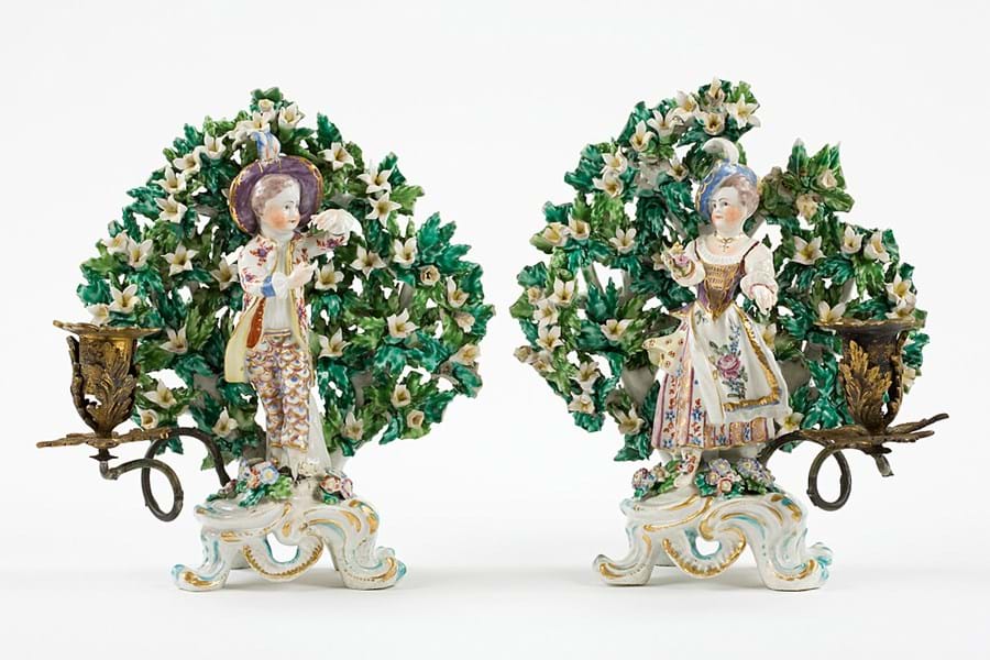 Ornate candlestick holders featuring figures of people against a floral backdrop