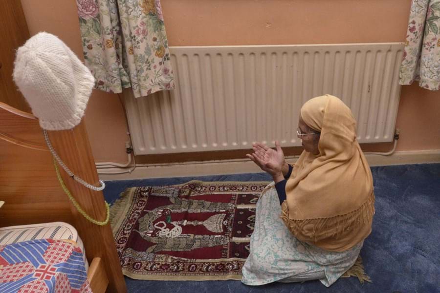A person wearing a headscarf kneeling on a carpet