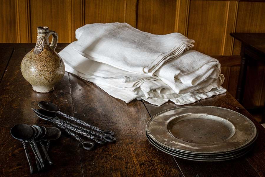 Black metal spoons, pile of pewter plates and ceramic drinking vessel
