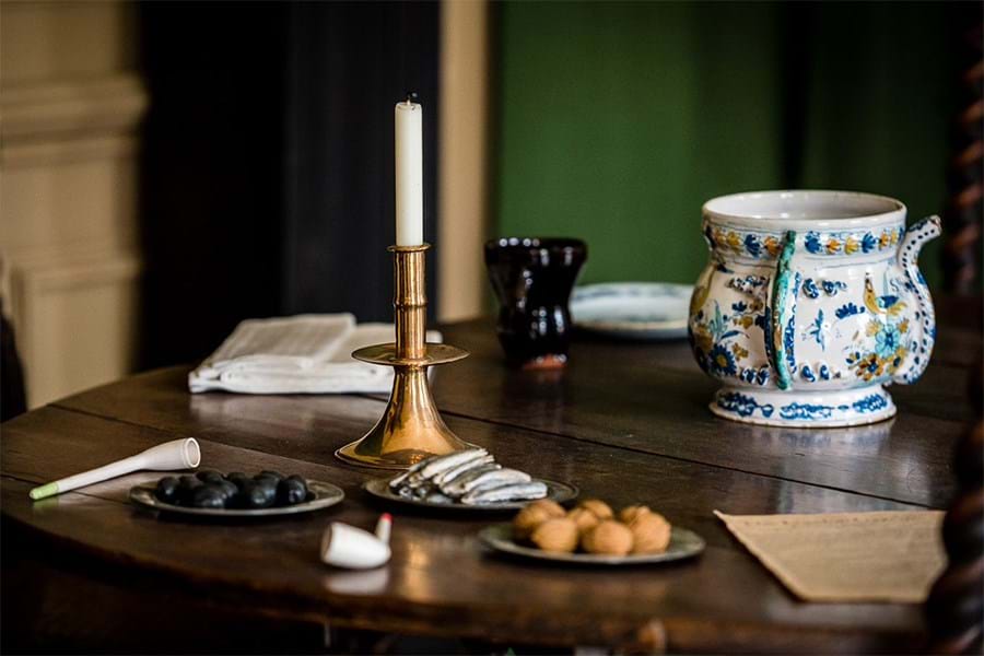 A wooden table set with a white and blue cup, small plates of nuts, a candle in a brass candlestick