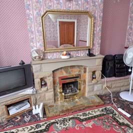 Pink wallpapered living with large mirror on a mantelpiece and large television set.
