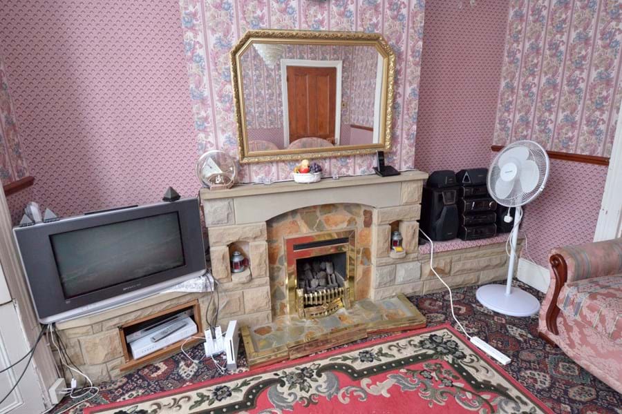 Pink wallpapered living with large mirror on a mantelpiece and large television set.