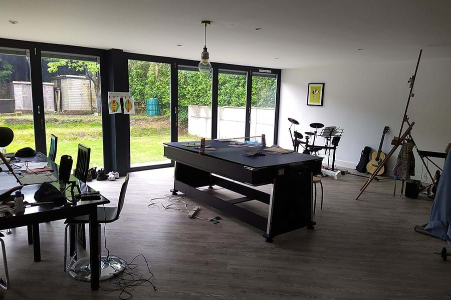 A room with a table and chairs set up and windows overlooking a lawn