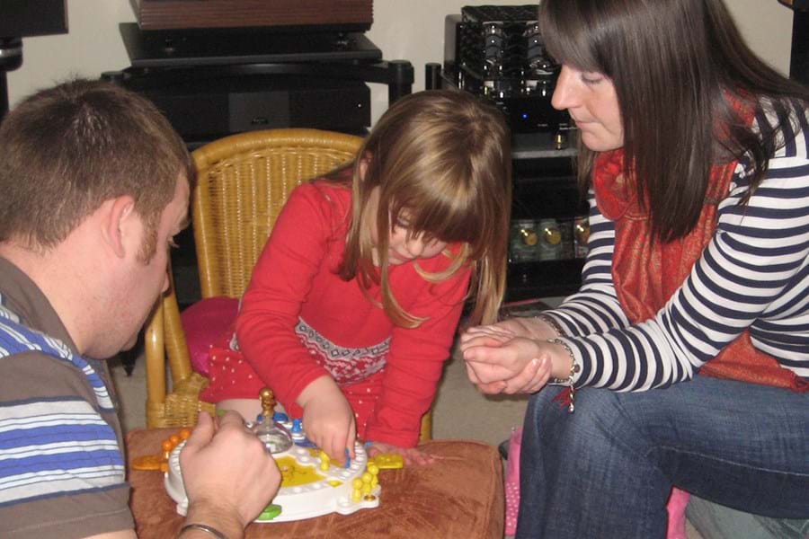 Two adults and a child playing a game with orange, yellow, green and blue pieces