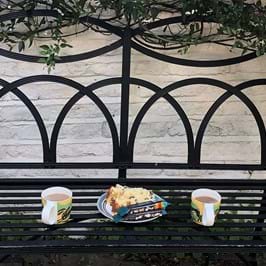 Two cups of tea and a slice of cake on a bench