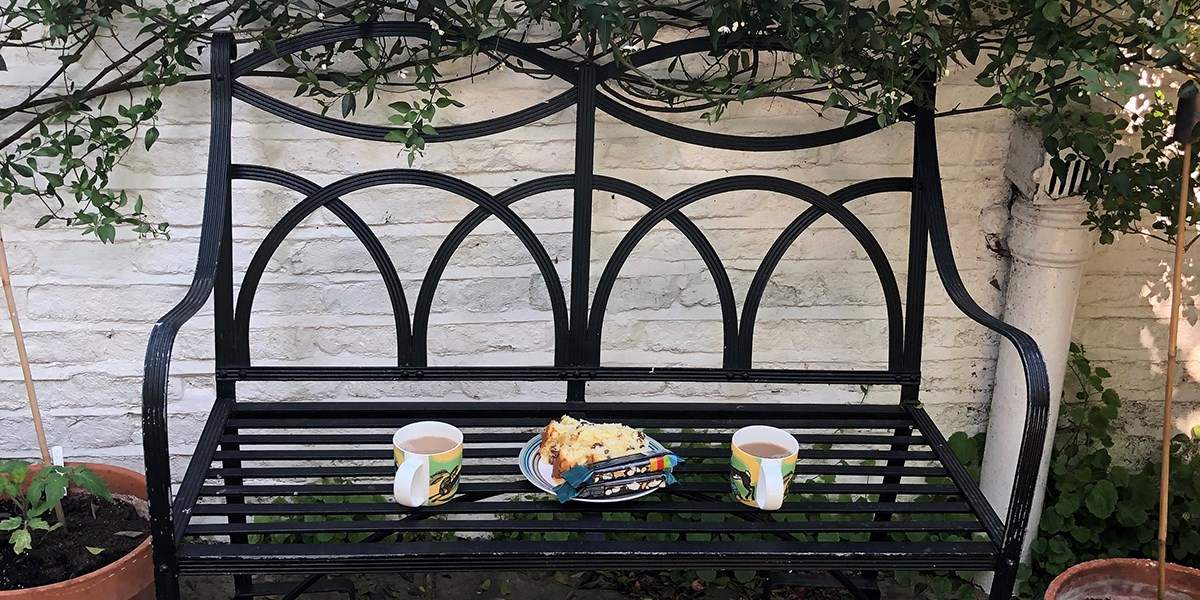 Two cups of tea and a slice of cake on a bench