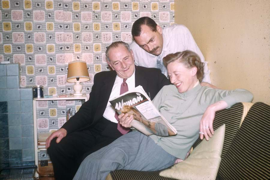 Three people reading a magazine on a sofa together with vibrant wallpaper behind them