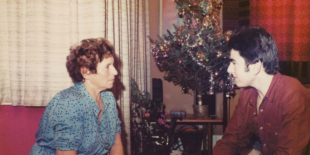 Two people sat on a sofa talking with a Christmas tree between them