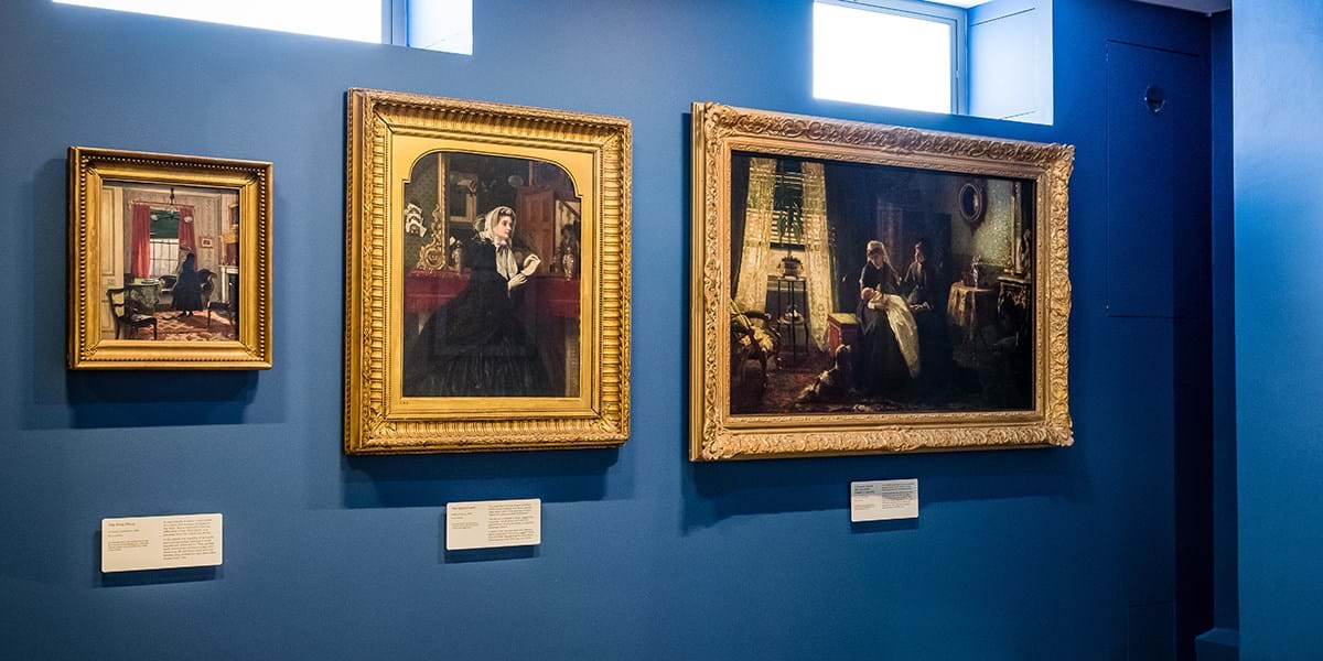 Three paintings in gold frames on a dark blue wall