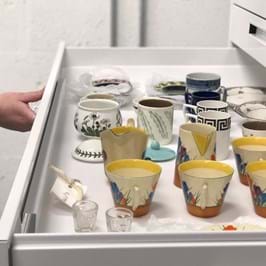A person holding open a drawer in the Museum stores to show a range of colourful cups and glasses 