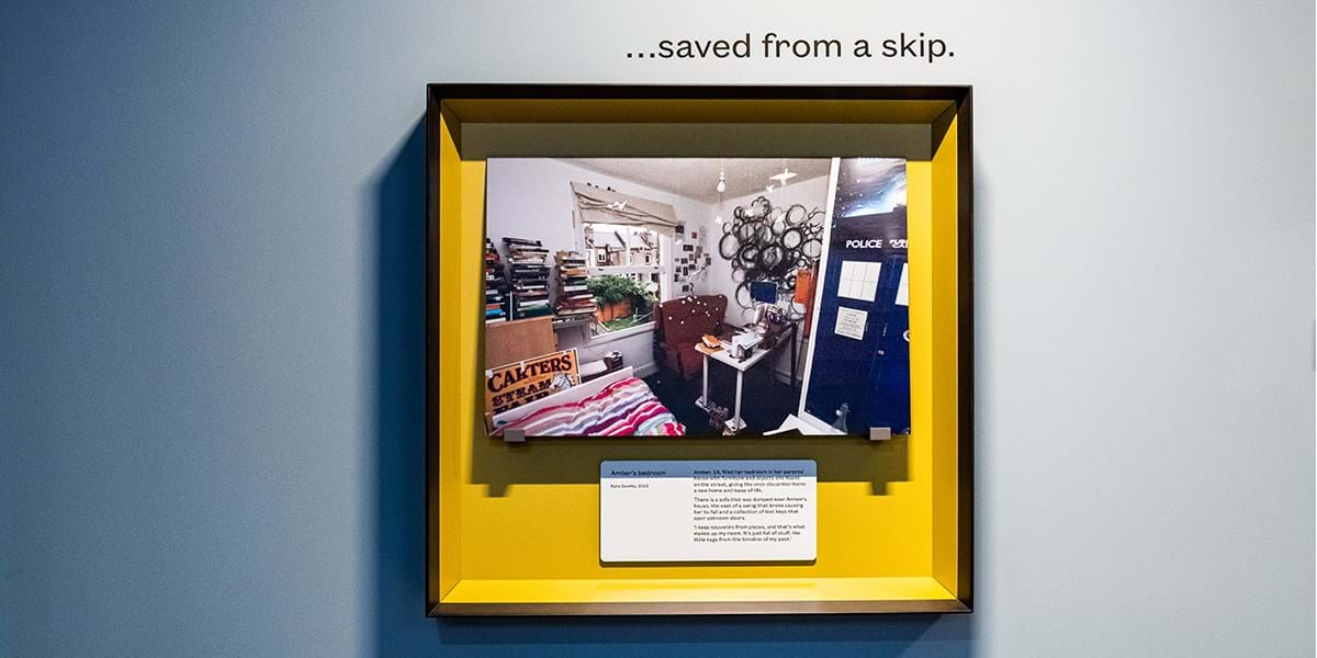 A photo of a bedroom inside a yellow square frame, with a black border, on a grey wall