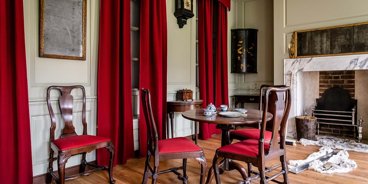 Room setting with four chairs, a table, red curtains, a fire place and various tools on the floor for cleaning