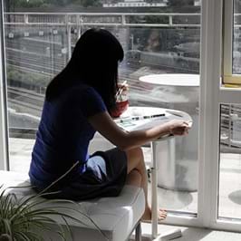 Person sitting while eating and reading in front of a window with view of train tracks