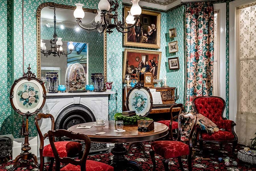 A room decorated in bright colours with a large mirror over the fireplace and a table and chair set