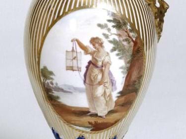 Close up of a painted vase depicting a person holding a bird in a cage