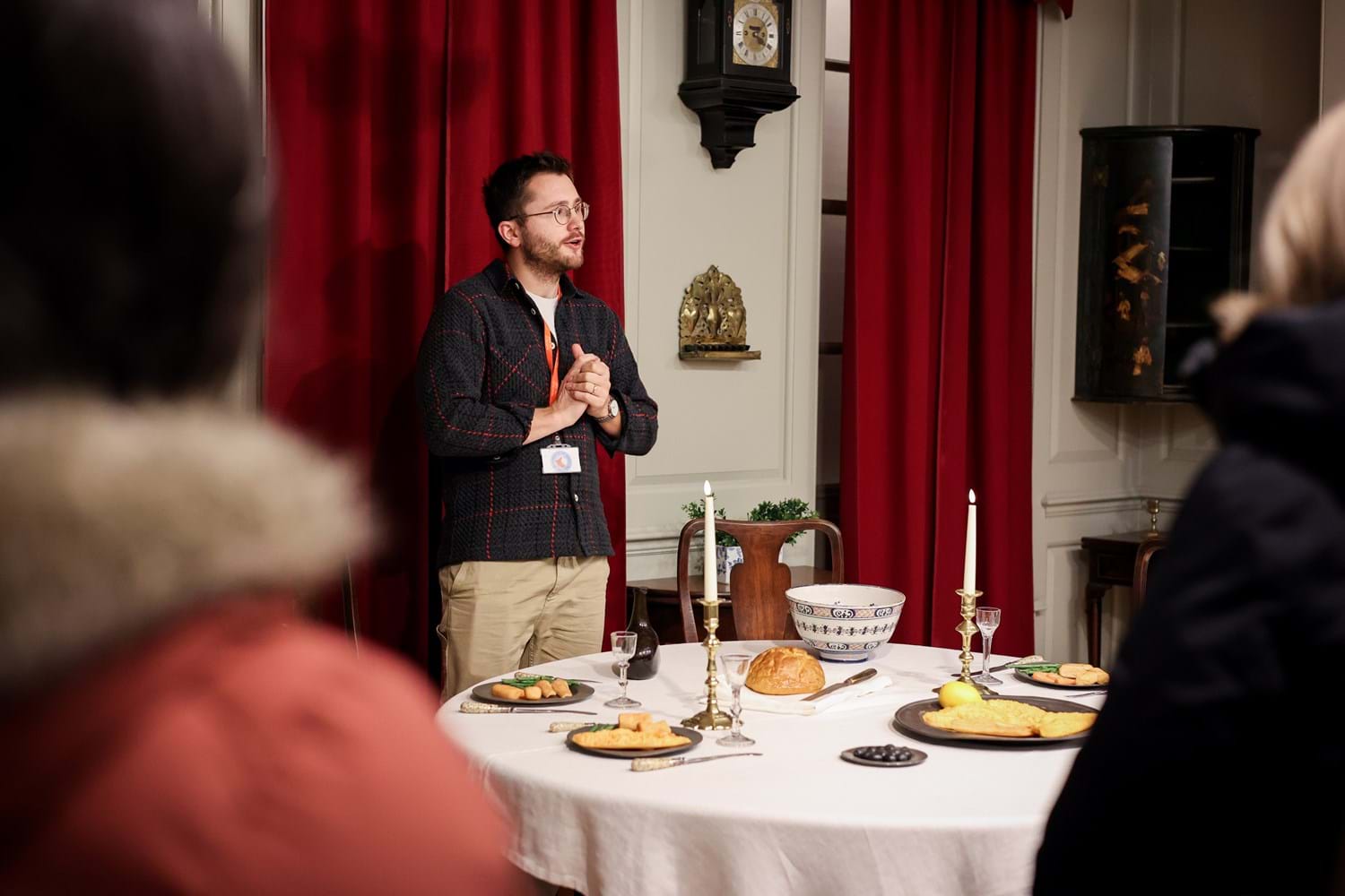 A person standing in front of a table set with foods for a candle lit supper while speaking to an audience