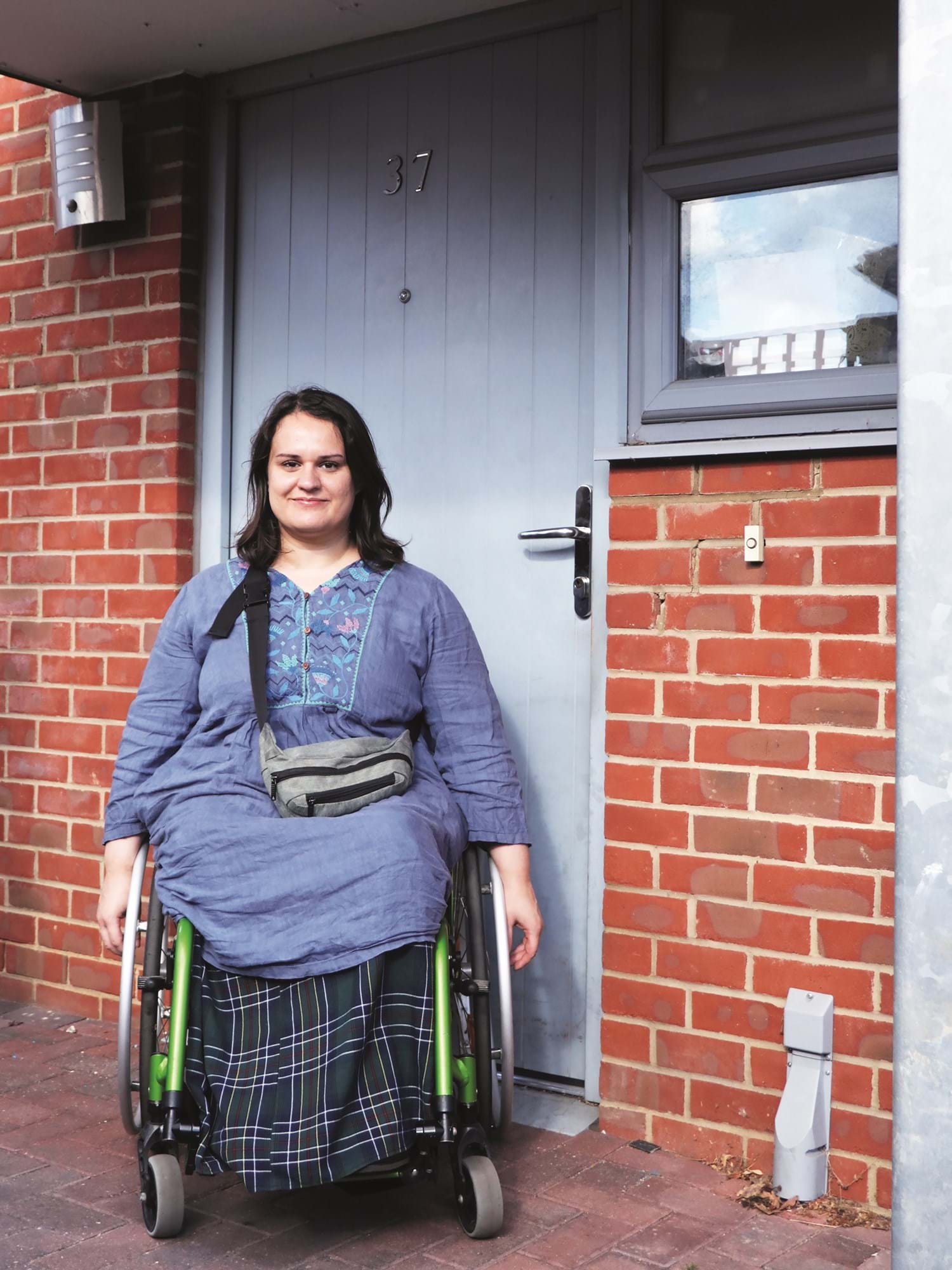 Person in a wheelchair smiling in front of a red brick wall and blue door 