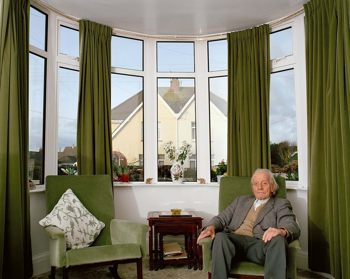 A person sitting on a green sofa in front of windows with green curtains