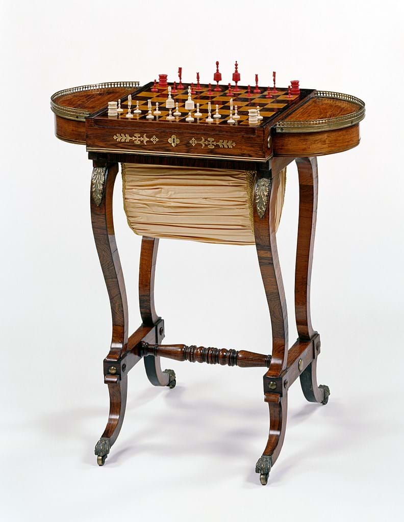 Wooden table fitted with chess board. Beneath the board is a beige bag in which to store the chess pieces. 