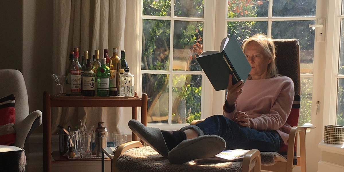 Person sat in chair reading a book in front of windows overlooking a garden