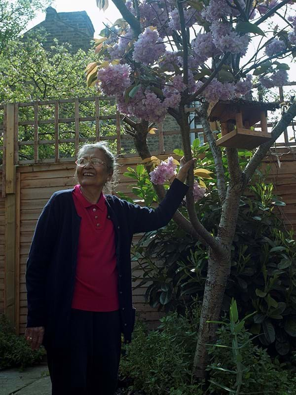 A person in a garden leaning on a tree 