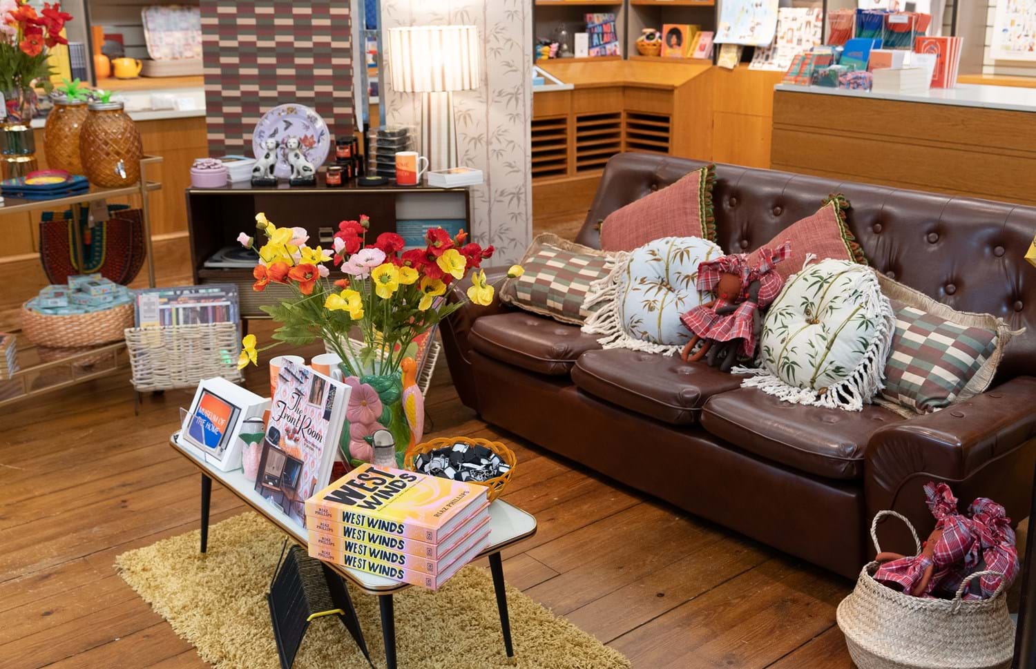 A brown leather sofa with floral throw pillows in natural tones surrounded by items from a museum shop on display