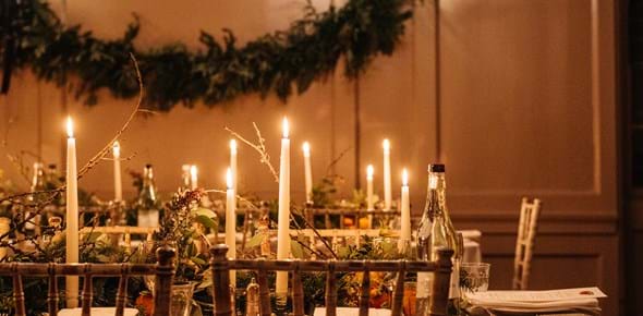 A candle lit table setting in a Georgian room, with greenery hung on the walls and on the table