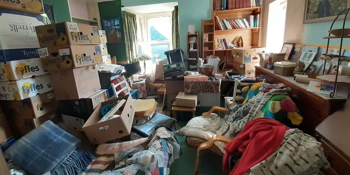 Room cluttered with various objects some in boxes and some on the furniture