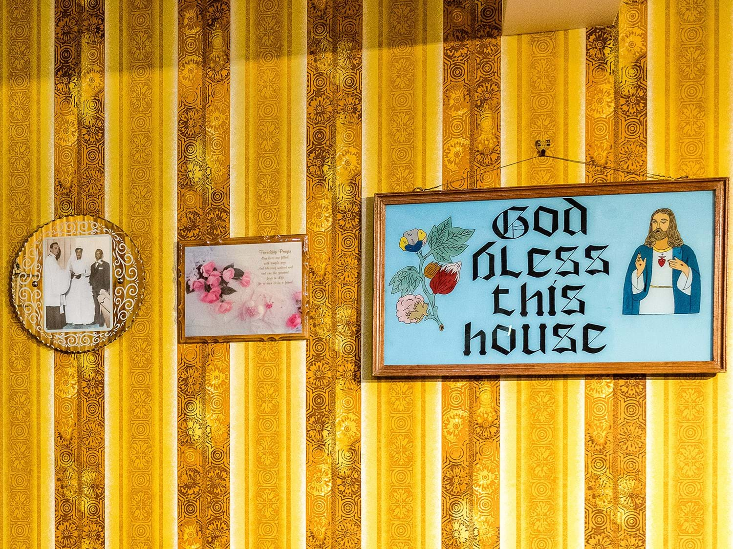 Yellow and brown striped wallpaper, with wall hangings including one reading God bless this house