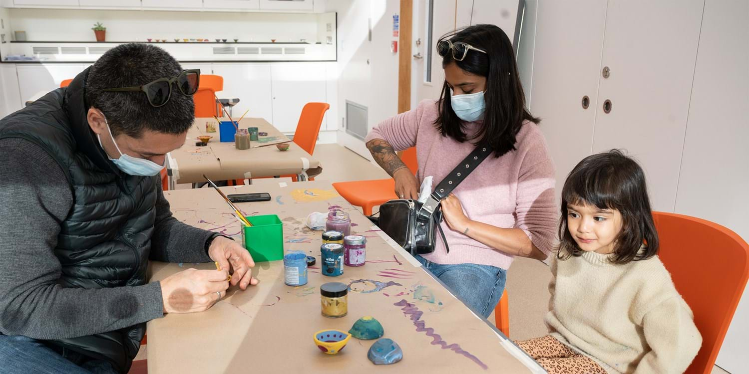 Two adults and a child doing craft activities at a table