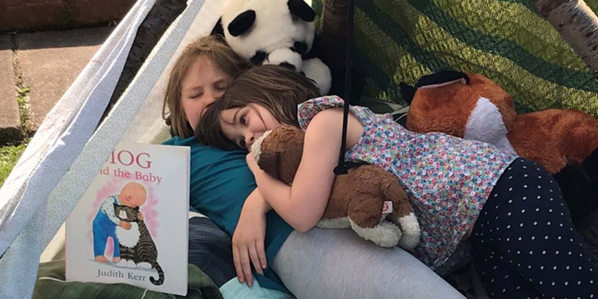 Children cuddling while reading a book in a tent
