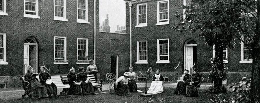 Black and white photograph of almshouse residents sat in the Kingsland Road Gardens
