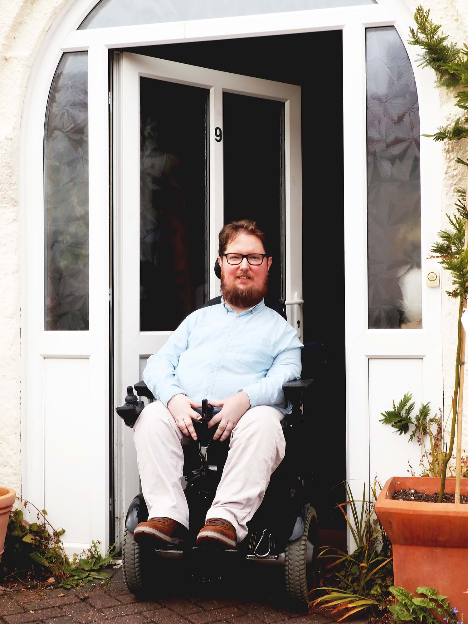 Photograph of a person in a wheelchair smiling outside a porch door