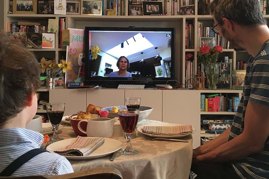 A child and an adult sitting at a table looking at a television screen for a video call with a relative