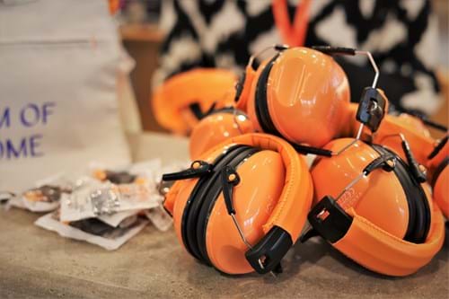 Several orange ear-defenders which resemble over-ear headphones, and foam ear plugs