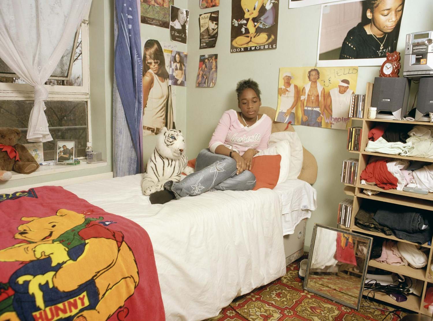 A young person sitting on their bed in a room decorated with posters