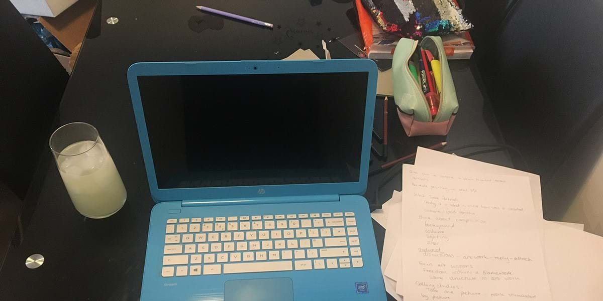 Open laptop with a glass of liquid on the left and papers on the right