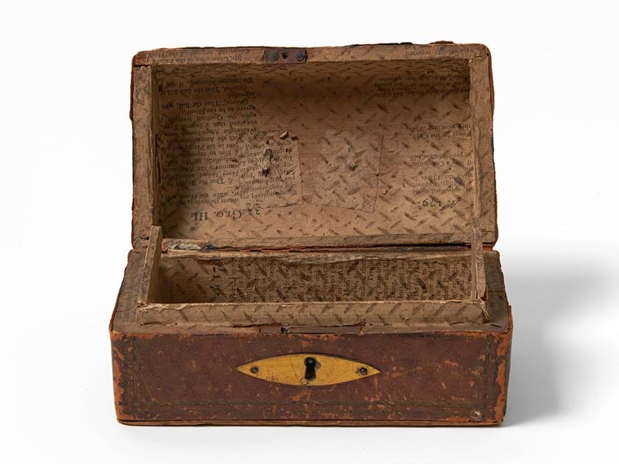 A leather covered box with printed paper lining and a gold lock